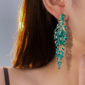 Close-up of model wearing luxury gold-toned teardrop tassel earrings with teal rhinestones
