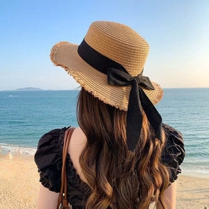 Flat top straw sun hat with frayed edge and black bow ribbon on a beach background