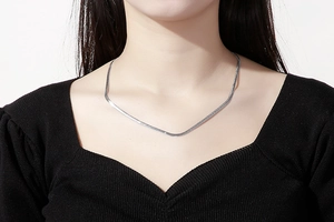 Détail d'un collier chaîne serpent minimaliste argenté porté par un mannequin en noir