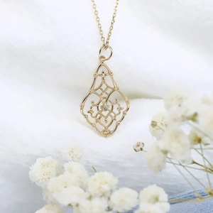 Dettaglio di un ciondolo geometrico dorato vintage con motivi floreali su tessuto bianco