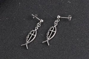 Detail of silver fish-shaped dangles with a cross and JESUS text on a black surface