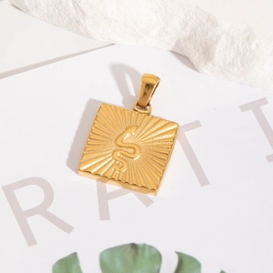 Détail d'un pendentif carré doré avec motif serpent en relief et texture rayonnante