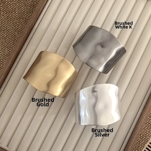 Detailed view of irregular brushed metal bangles in gold, silver, and white finishes