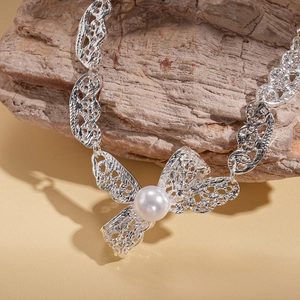 Macro view of silver hollow lace necklace with a white pearl on a wooden base