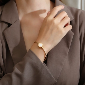 Detail of gold roman numeral bangle with white shell inlay on a model sleeve