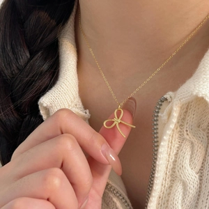 Close-up of golden bow pendant with rope texture worn on a cream knit sweater