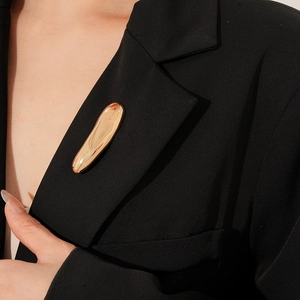 Detail of a minimalist gold lava-shaped brooch styled on a dark blazer lapel for women