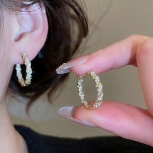 Gros plan de boucles d'oreilles créoles dorées avec pavé de zircon et nacre de perle