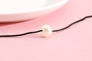 Macro shot of single white pearl on a black cord necklace with minimalist detail