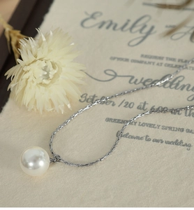 Elegant single pearl pendant necklace on silver chain over a romantic wedding invite