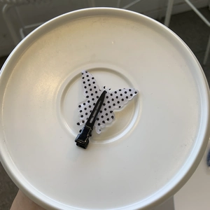 Detail view of a black and white polka dot bow hair clip with a metal duckbill base