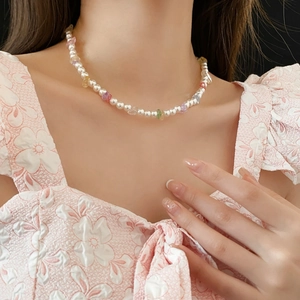 Close-up of pearl necklace with colorful gemstones worn on a model neckline