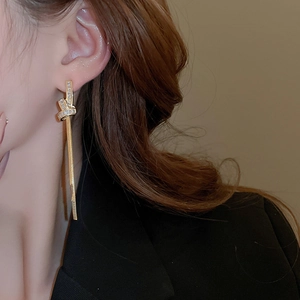 Close-up of model wearing long gold tassel knot earrings with sparkling zircon stones