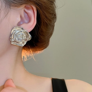 Primo piano di un orecchino a rosa d'argento con petali metallici stratificati su modella