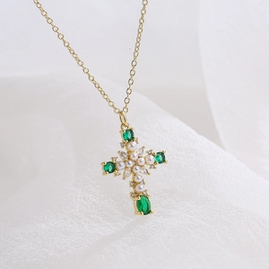 Golden cross necklace with green oval gemstones and pearls on white fabric background