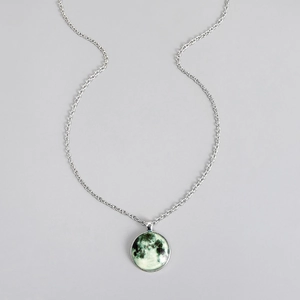 Close-up of a silver luminous space planet pendant necklace with textured green moon