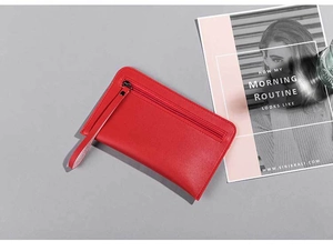 Detail of red leather clutch bag with black nickel hardware and wrist strap on gray backdrop