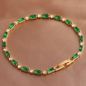 Detail of a golden bracelet with green emerald-cut and clear round cubic zirconia stones