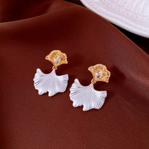 Macro detail of golden ginkgo leaf earrings with zircon and white pearlescent petals