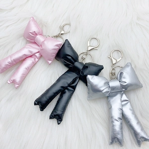 Puffy shiny bow keychains in pink, black, and silver colors on soft plush background