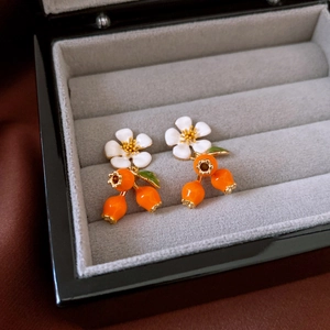 Detailed close-up of white enamel flower earrings with vibrant orange fruit drops