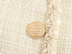 Vue détaillée du tissu tweed crème avec bouton doré et finition à franges
