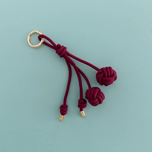 Detail of dark red hand-woven volleyball charm with elegant golden spring clasp