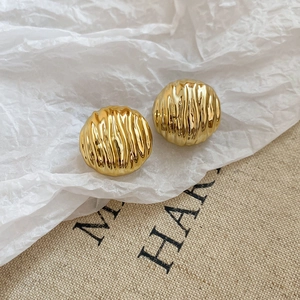 Detail view of round golden metal stud earrings with unique vertical textured pleats