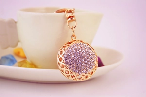 Close-up of golden keychain with purple rhinestones on a white ceramic coffee cup rim