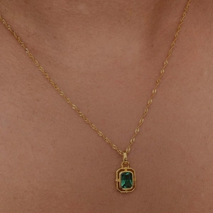 Detail showing a golden twisted chain necklace with a rectangular green zircon pendant on skin