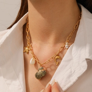 Gold necklace with green conch shell and starfish dolphin charms on model's neck