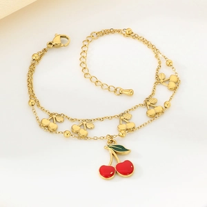 Close-up of a double-layered 18K gold chain bracelet featuring red enamel cherry pendants