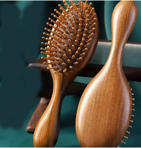 Detailed view of two brown sandalwood massage hairbrushes on a green fabric backdrop