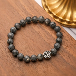 Dettaglio di bracciale con pietre e ciondolo ad ancora d'argento su fondo di legno