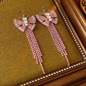 Dettaglio di orecchini vintage a farfalla con nappe e zirconi rosa su fondo di velluto