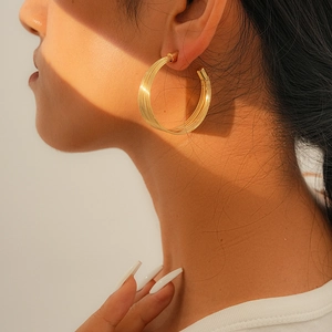 Nahaufnahme eleganter goldener mehrlagiger Creolen, getragen von einem Modell im Sonnenlicht