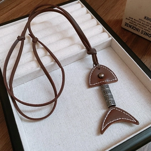 Close-up of vintage brown leather and metal fishbone pendant on a soft velvet display