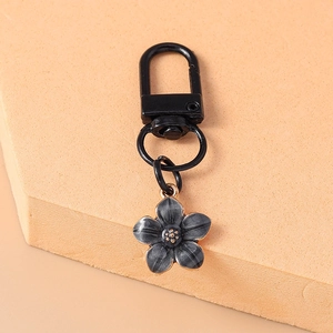 Close-up of a vintage black metal keychain featuring a grey flower pendant and gold details