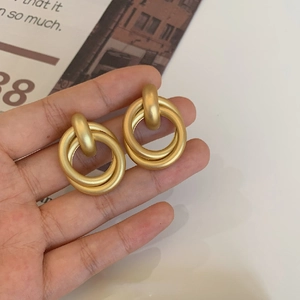Close-up of interlocking matte gold geometric hoop earrings held by hand to show detail