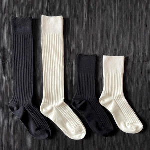 Detail of black and white ribbed knit knee-high and ankle socks on pleated fabric