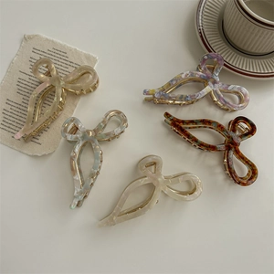 Bow-shaped acetate hair claws in five colors including beige, amber, and blue on desk