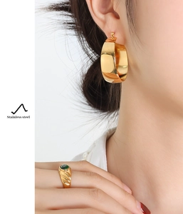 Detailed view of 18K gold plated stainless steel U-hoop earrings and green gem ring