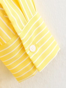 Close-up of yellow and white striped shirt cuff with a white button on twill fabric