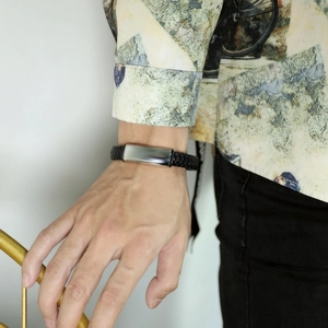 Dettaglio del bracciale da uomo in pelle nera intrecciata con placca in metallo lucido