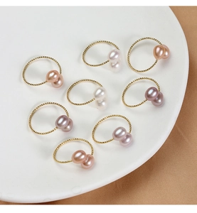 Detailed view of dual natural freshwater pearls on gold braided open rings in various colors