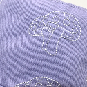 Gros plan sur la broderie de champignon argenté du chapeau bob en sergé de coton lilas