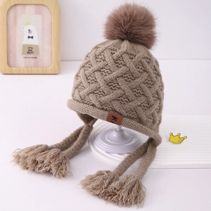 Close-up of knit earflap hat with chunky texture, faux fur pompom and tassel straps