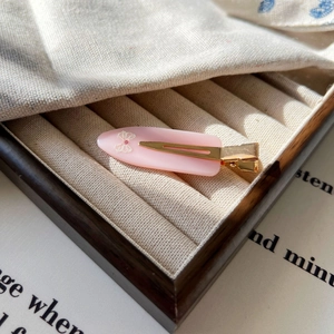 Détail d'une pince à cheveux en acétate rose avec motif nœud blanc et petit strass rose