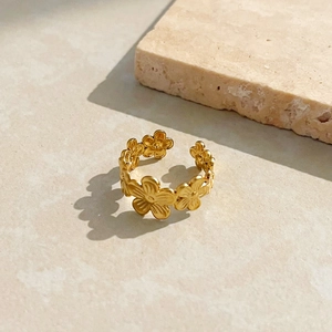 Artistic close-up of an 18K gold floral open ring on a textured stone background