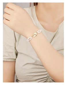Dettaglio del bracciale a doppio strato di perle bianche con maglia dorata al polso donna